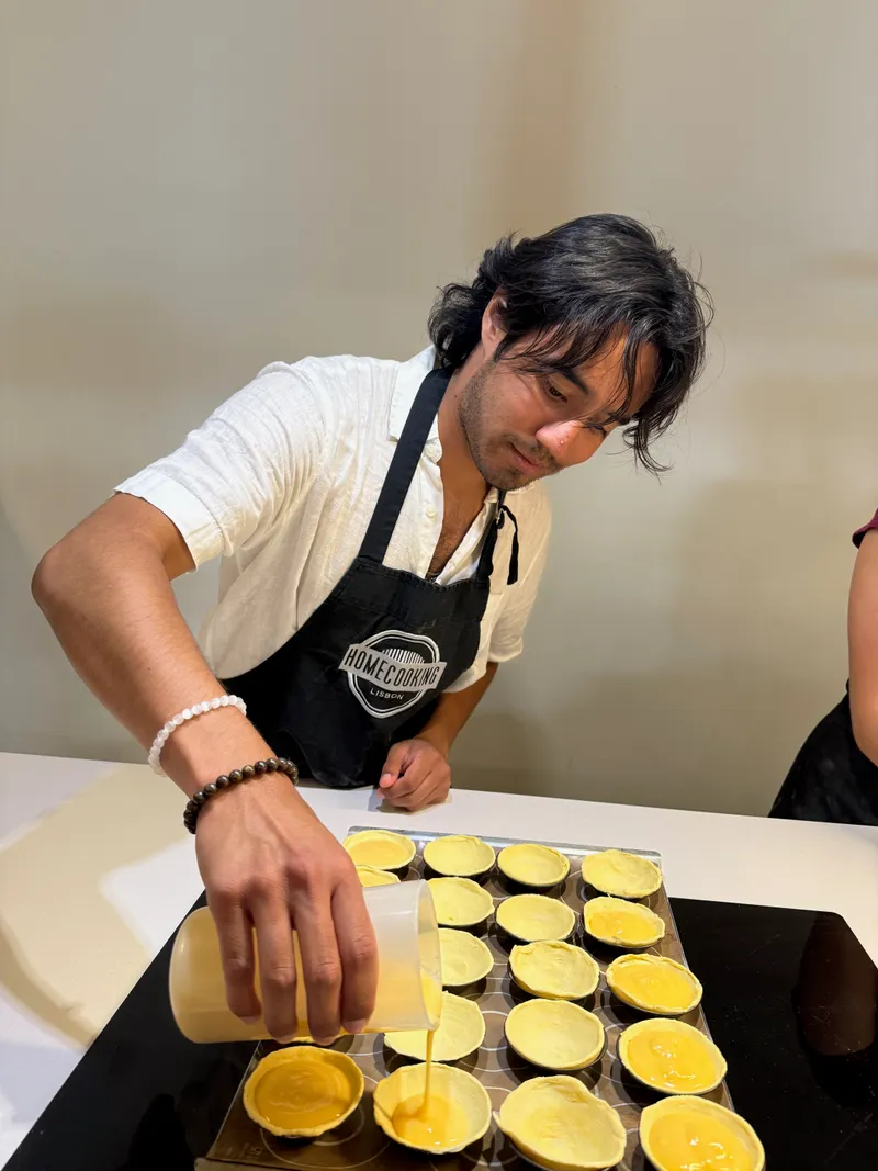 Karl in a Home Cooking Lisbon apron, pouring custard into pastry shells during a pasteis de nata cooking class
