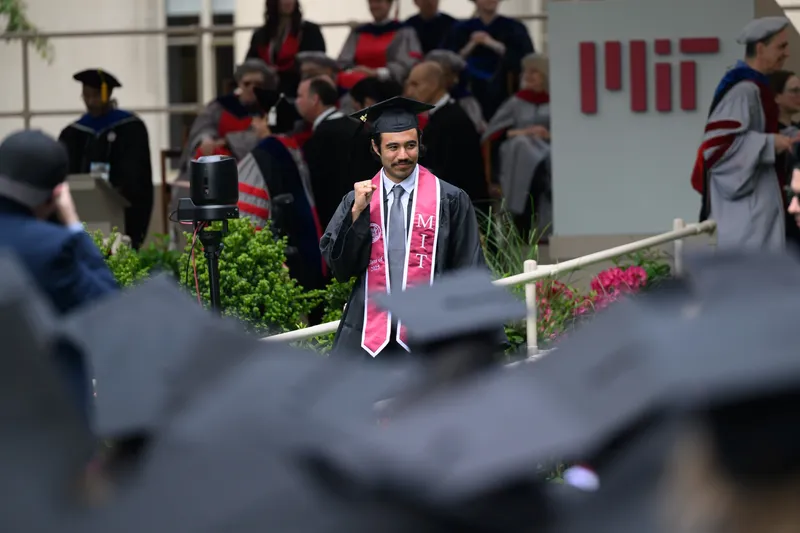 Karl pumping his fist while walking past a large MIT sign at graduation