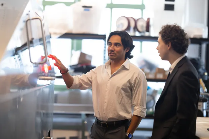 Karl gesturing toward a control panel while demoing hardware to a colleague in the workshop