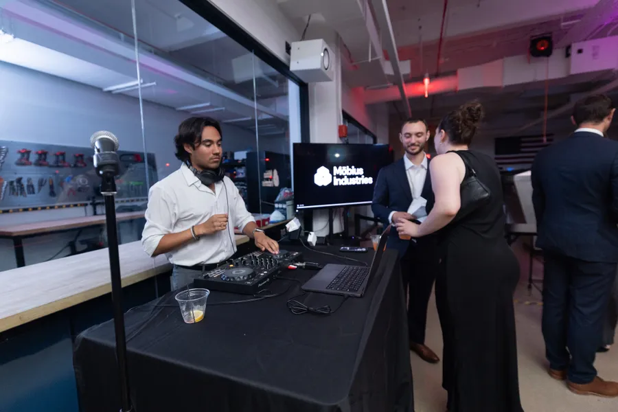 Karl DJing at the Mobius Industries gala with guests chatting nearby