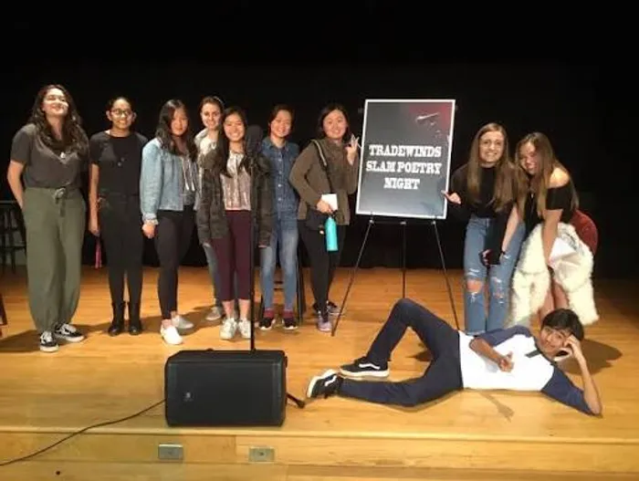 A group of high school students posed on stage with a younger Karl lying on the ground in front making a joking pose